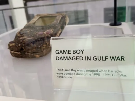 A burnt Game Boy sits in a glass case in a museum.