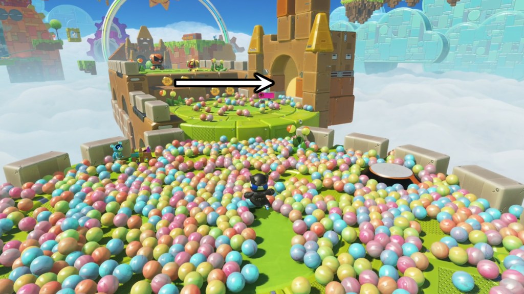 Astro Bot in a multicolored ball pit with an arrow pointing to a hidden bot.